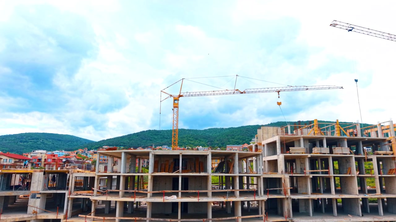 Cantiere per la costruzione di una struttura in cemento armato a più piani con gru. Scheletro di un grande edificio in costruzione con una gru a torre gialla sullo sfondo di colline e una città.