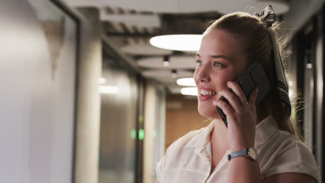 talking on smartphone, businesswoman in modern office hallway, focusing on conversation