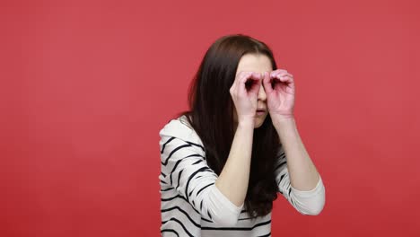retrato de una mujer espiando mirando a través de agujeros en sus manos, haciendo binoculares, sorprendida por lo visto.