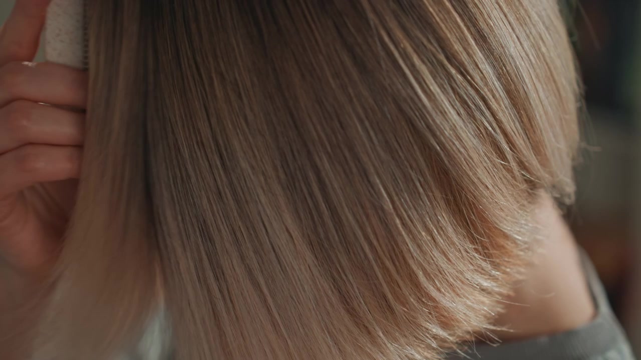 Mujer caucásica amante de la música ajustándose el corte bob en un primer plano casero, manos colocando el cabello rubio detrás de la oreja, iluminación cálida y suave, suéter acogedor, expresión contemplativa, bokeh cinematográfico, momento íntimo de arreglo personal