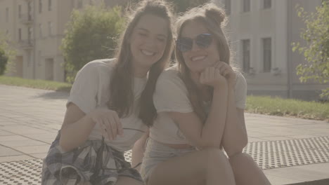 two happy women sitting on a sidewalk