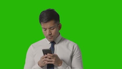 Foto-De-Estudio-De-Un-Hombre-De-Negocios-Serio-Con-Camisa-Y-Corbata-Usando-Un-Teléfono-Móvil-Contra-Una-Pantalla-Verde