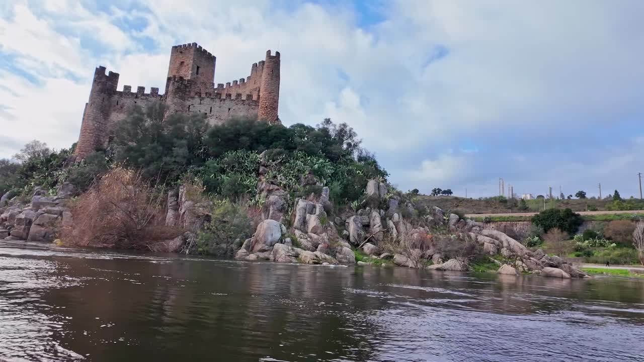 Vista da una barca che passa il Castello di Almourol sul fiume Tago vicino a Vila Nova da Barquinha, Portogallo, mostrando la fortezza medievale su un'isola rocciosa sotto un cielo nuvoloso