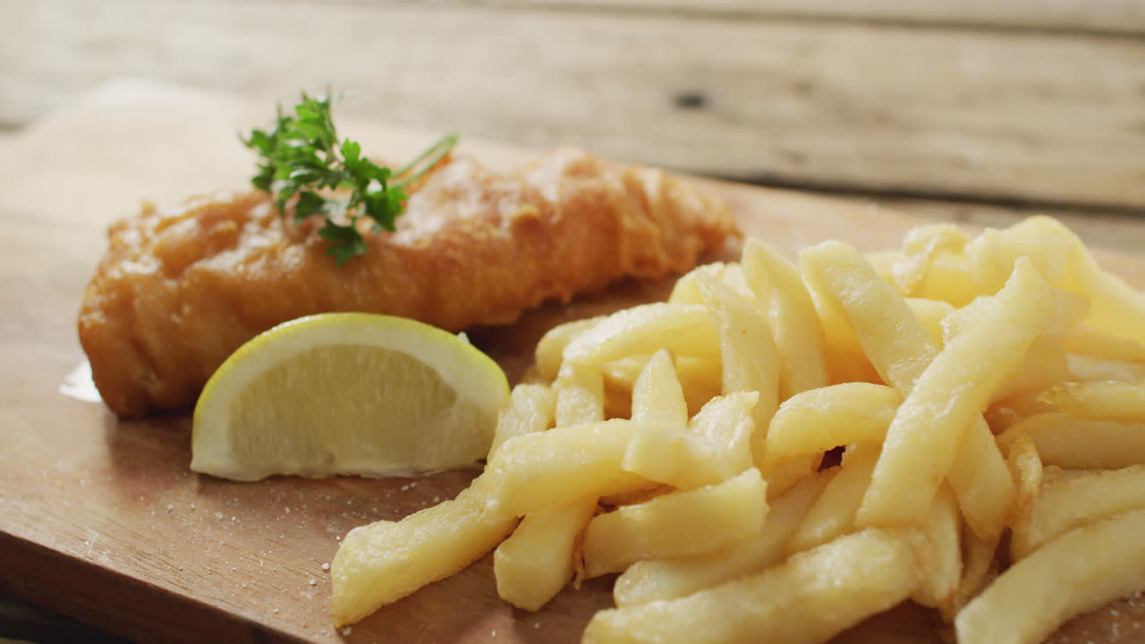 Video of fish and chips with lemon wedge on wooden board, on rustic table