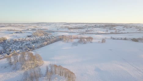 Paisaje-Invernal-Con-Un-Pueblo-Con-Grandes-Casas-Y-Campos-Cubiertos-De-Nieve-Blanca-Y-Una-Carretera-Asfaltada-Despejada-En-Un-Día-Frío-Y-Brillante-En-Escocia-Durante-La-Hora-Dorada