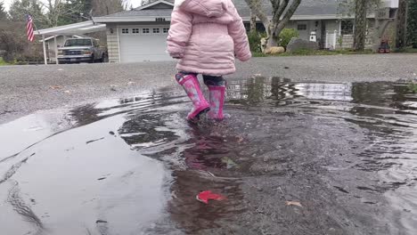 close up of a little girl walking through a large puddle wearing pink rubber boots