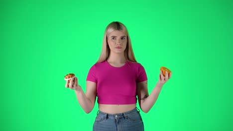 young woman holding muffin pastry and orange slice, healthy and unhealthy food, green background studio shot