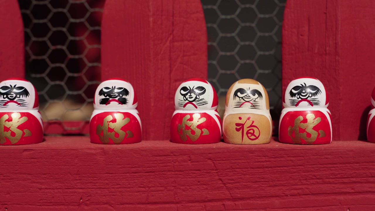 Fila di bambole Daruma rosse e bianche con kanji dorati su una mensola di legno rossa in un santuario giapponese in Giappone.