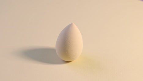mezclador de belleza de esponja cosmética en un fondo beige giratorio.