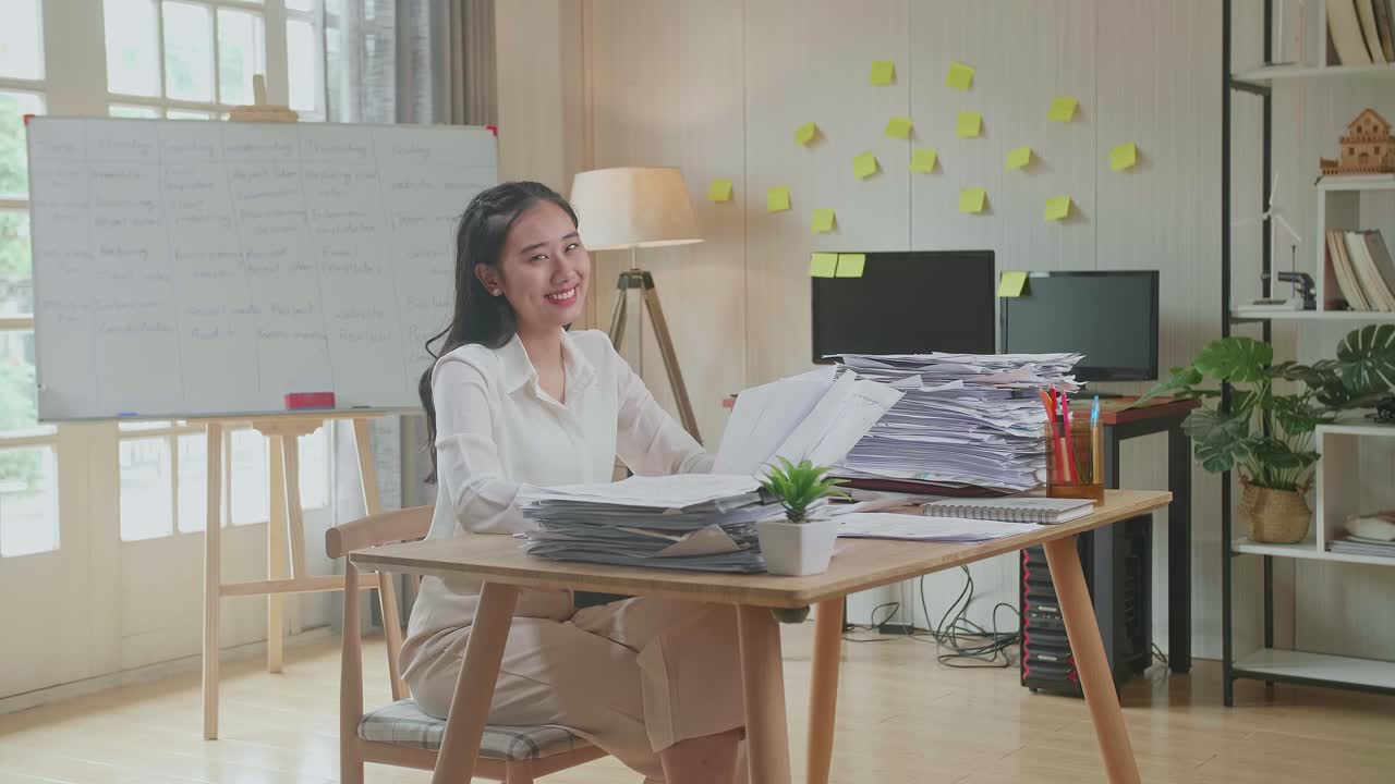 Asian Woman Smiling To Camera While Working With Documents At The Office