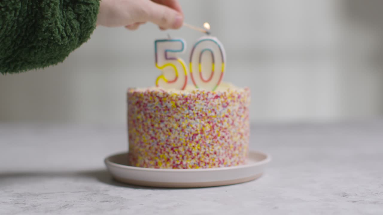 студийный снимок праздничного торта, покрытого украшениями, и зажженной свечи в честь пятидесятого дня рождения