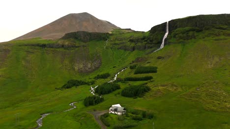 witness the power of nature as our drone captures the stunning waterfall of bjarnarfoss, framed by towering peaks and lush greenery in the heart of iceland