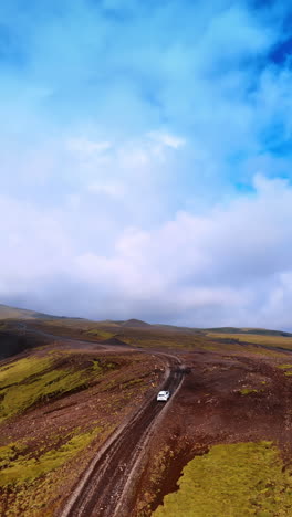 Car goes by the ground road passing by the rocky landscape. Mountainous panorama of Iceland and bare ground with some moss. Top view. Vertical video.