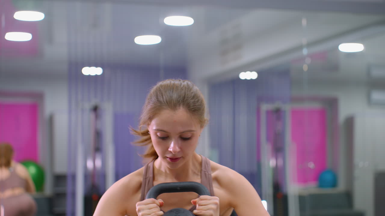 젊은 여성이 무게를 들어 올리고, 높은 표면에 발을 고, 그 다음에 아래로 내려와 체육관에서 다시 무게를 들고, 근력 훈련, 균형, 그리고 체력 훈련에 초점을 맞추고, 배경에는 체육 장비가 있습니다.