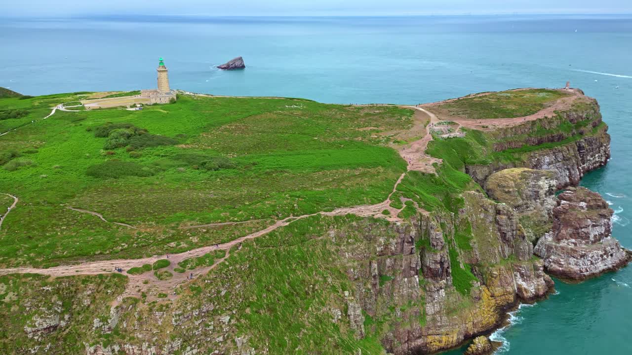 Drone flies inland from sea toward Cap Fréhel lighthouse, showing cliffs, trail, greenery, and surrounding ocean. Brittany, France