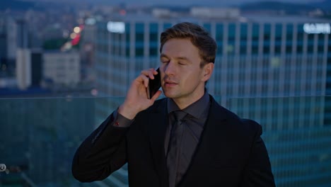 confident businessman in a suit talks on phone atop city rooftop terrace with skyscraper view during sunset