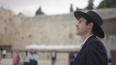 jewish religious man at the western wall, jerusalem, israel. he walks in black suit and black hat in front of the wall in selective focus and slow motion.