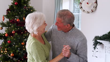 romantic senior couple dancing together at home with christmas tree in background