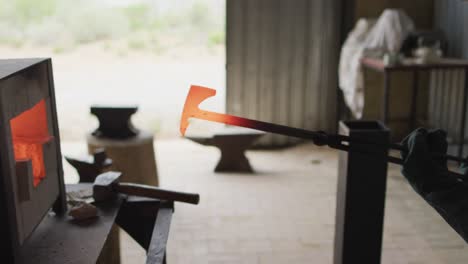 caucasian male blacksmith holding hot metal tool in kiln with tongs in workshop