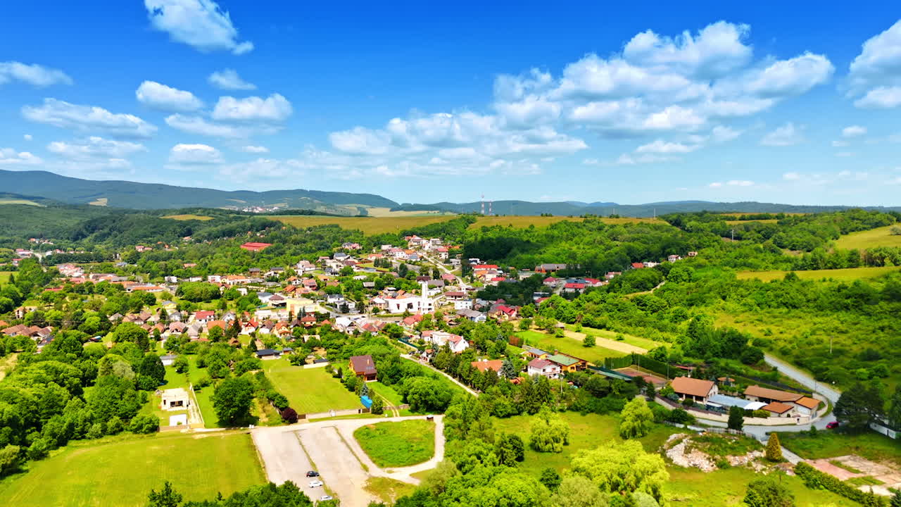Colorful village in green hills. A picturesque European village nestled in lush green hills under a bright blue sky, showcasing its natural beauty