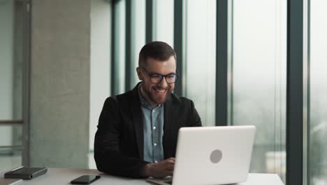 A-cheerful-man-sitting-at-a-laptop-begins-to-laugh-at-what-he-saw