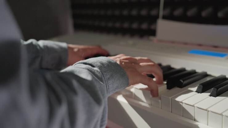 An elegant shot of a hand wearing a blue sleeve shirt playing the piano, featuring a blurred background that highlights the artist's focus