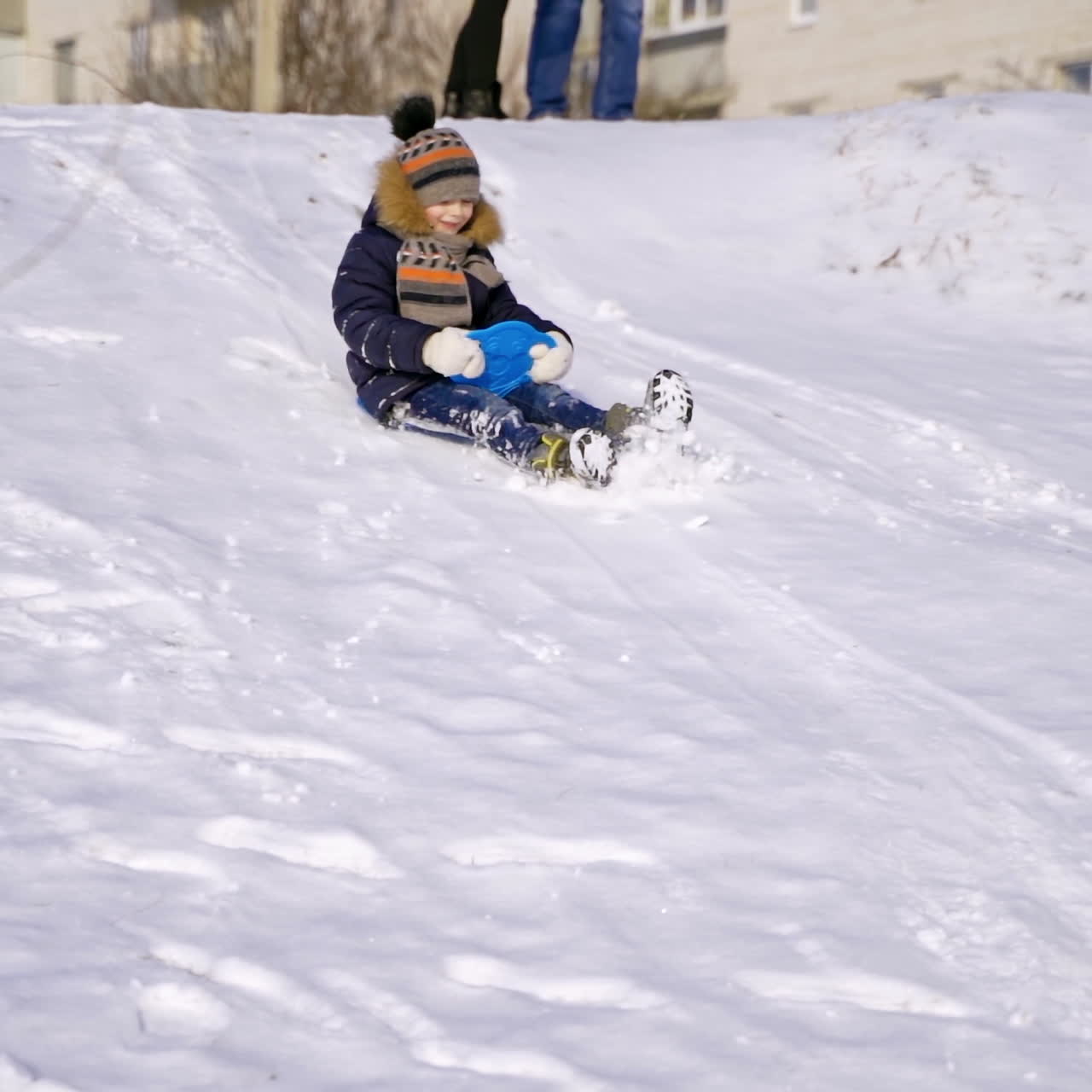 Boy on a snow slides. Little child sledding on plastic sled happily from the white hill in winter. Slow motion.