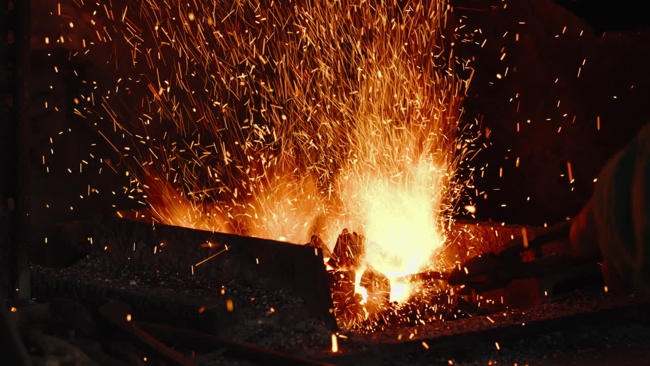 Close-up of a blacksmith's hand, using tongs on a piece of metal, stirring up the fire of the coal forge