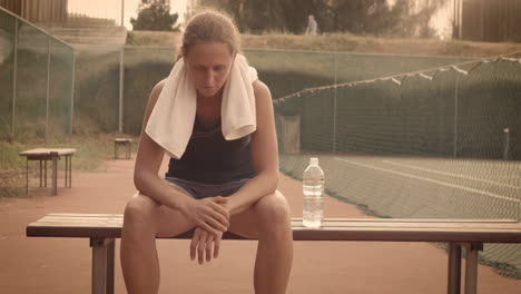 tired female tennis player resting on a bench on the court