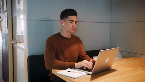 Young-man-working-alone-on-a-laptop-at-a-table-in-a-booth-at-an-office-canteen,-zoom-out