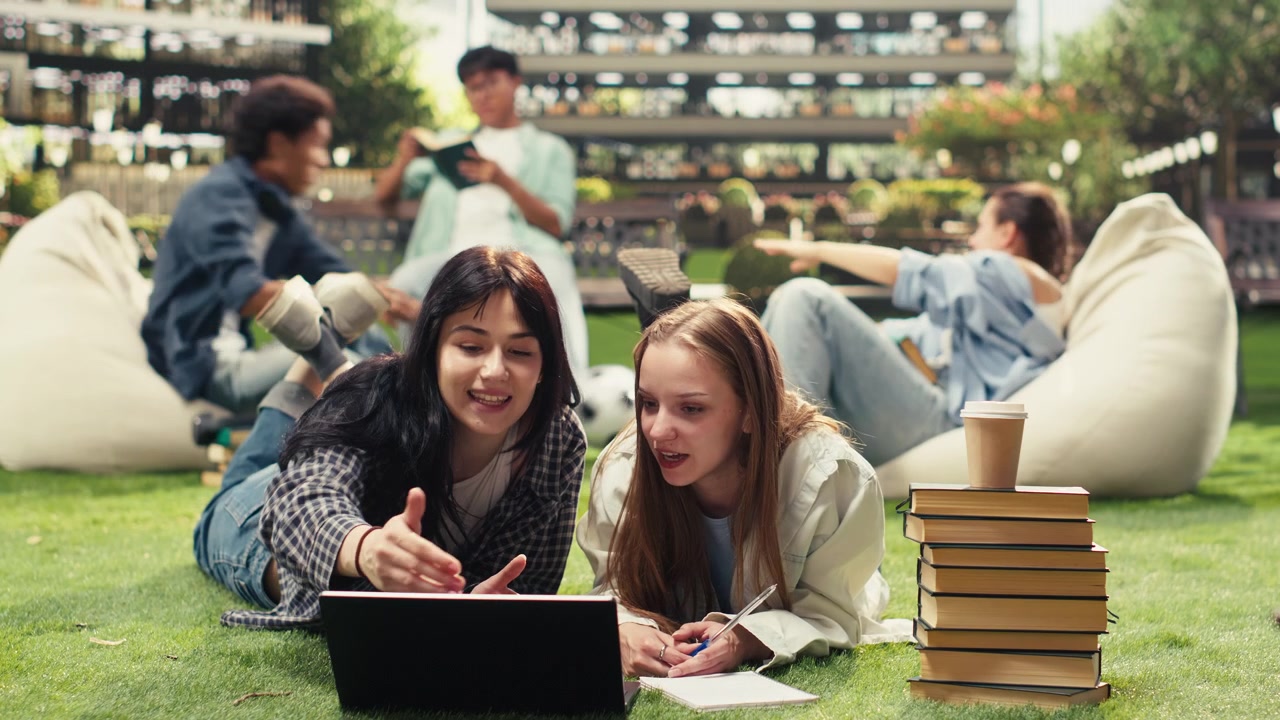 Students laying and leaning over open laptop and study materials