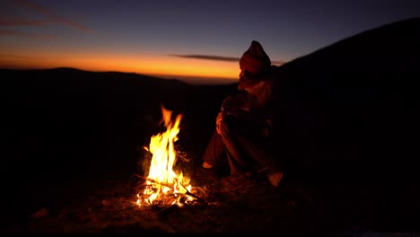 young man enjoys a campfire alone in nature at sunset after hiking