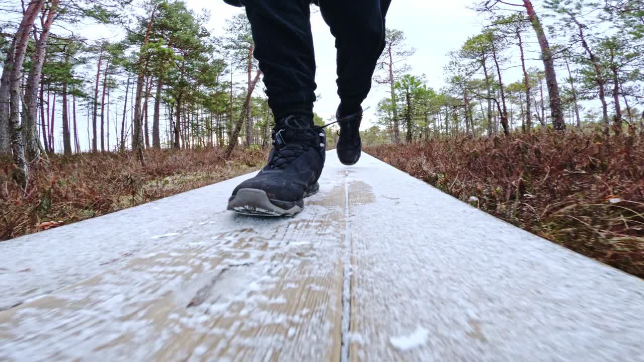 Man in black steps carefully on frosty wooden boardwalk in marshland slow motion