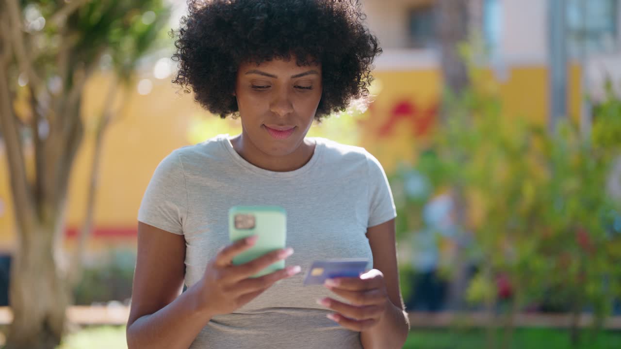 Young african american woman using smartphone and credit card at park