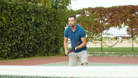 hombre guapo jugando al tenis y golpeando la pelota con raqueta en un día de verano en la cancha deportiva