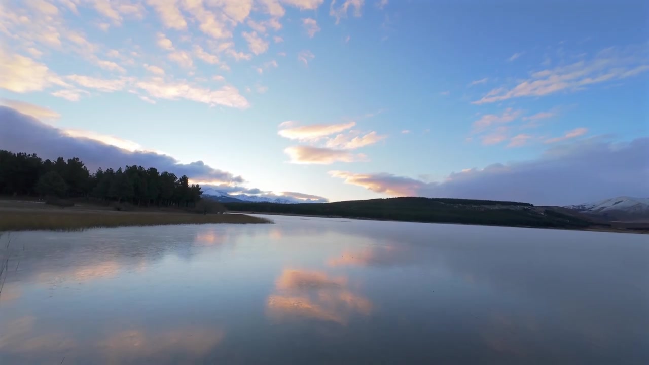 Esquel'deki Laguna La Zeta'nın sakin suları üzerinde, gökyüzü yansımaları içeren ahşap bir iskele ve kameriyenin yanından drone uçuşu