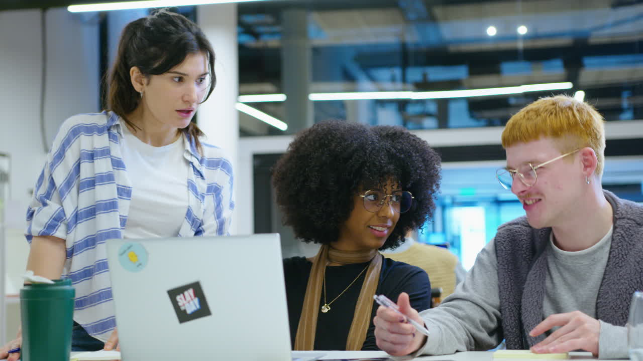 Team of Young Cheerful Coworkers Smiling and Discussing Project on Laptop