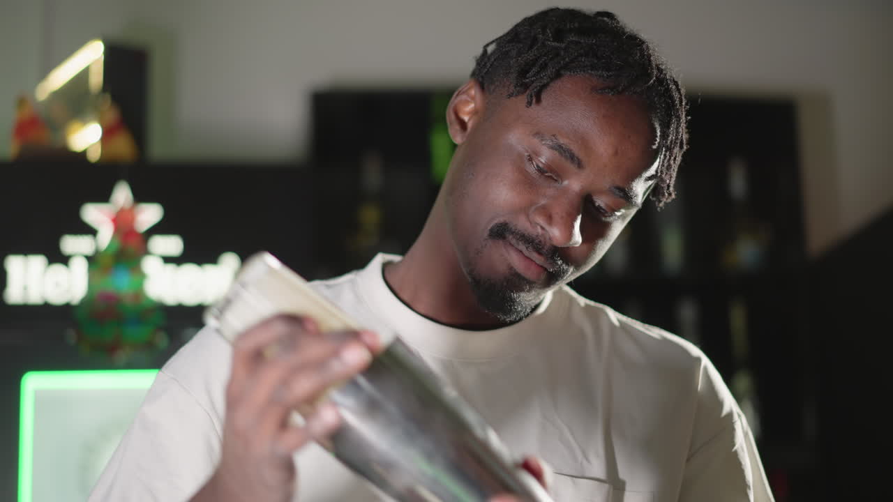 Bartender shaking cocktail in shaker, smiling while mixing drinks, neon lights at bar setting creating a vibrant atmosphere