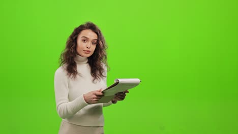 la mujer está hojeando los documentos y buscando la información necesaria. está levantando la cabeza y mirando a la cámara. está de pie sobre un fondo verde. pantalla verde. 4k.