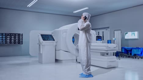 full body side view of asian male scientist talking on smartphone while standing with mri machine in the hospital