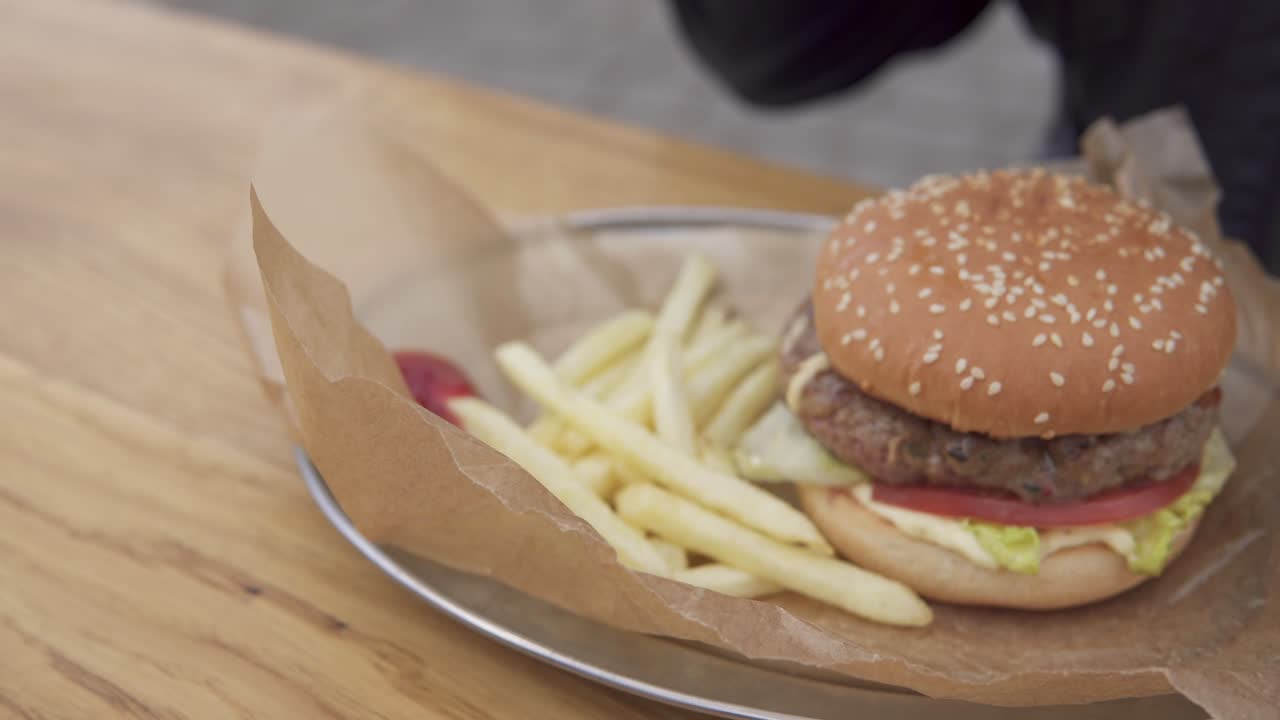 Tasty burger with french fries on the plate. Man's hand putting potato in ketchup and eating. Shot in 4k