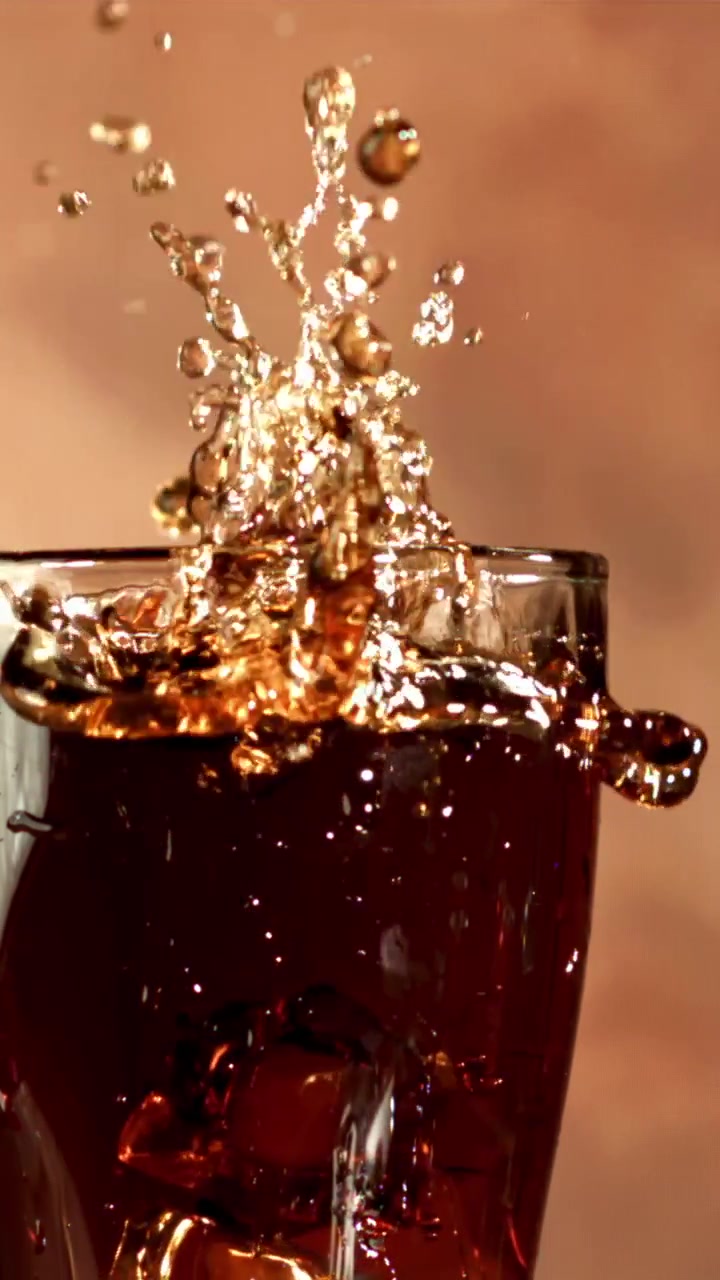 Cubetto di ghiaccio che schizza in un bicchiere di cola al rallentatore.