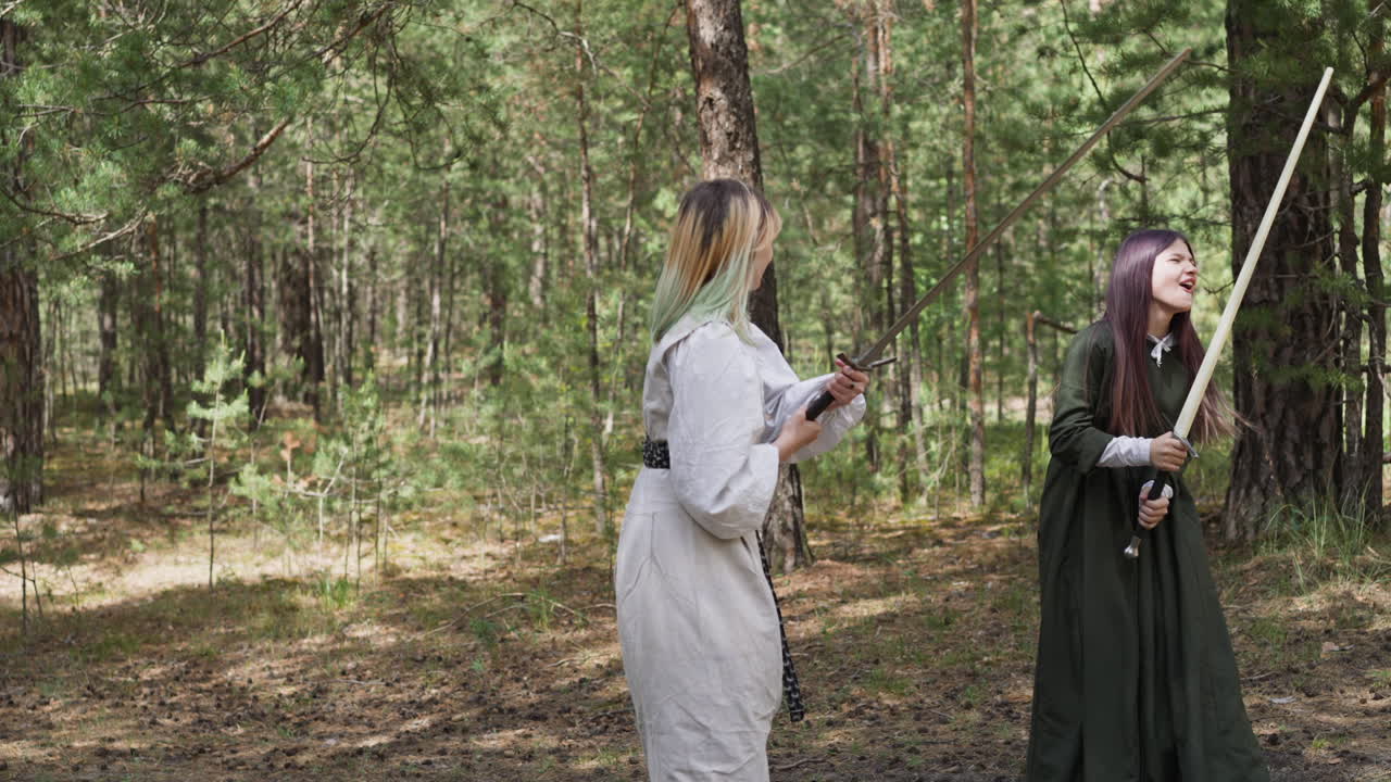 ролевые девушки в старинной одежде сражаются на мечах в дереве
