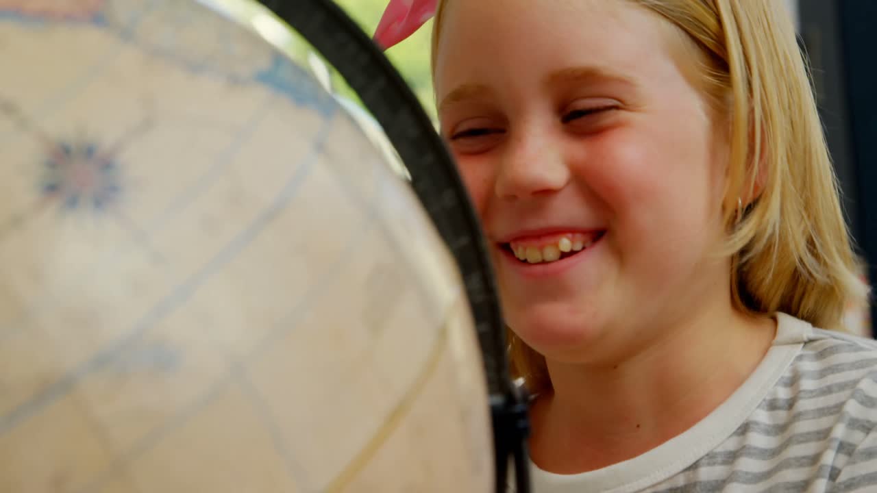 vista frontal de una feliz colegiala caucásica estudiando el globo en el escritorio en el aula de la escuela 4k