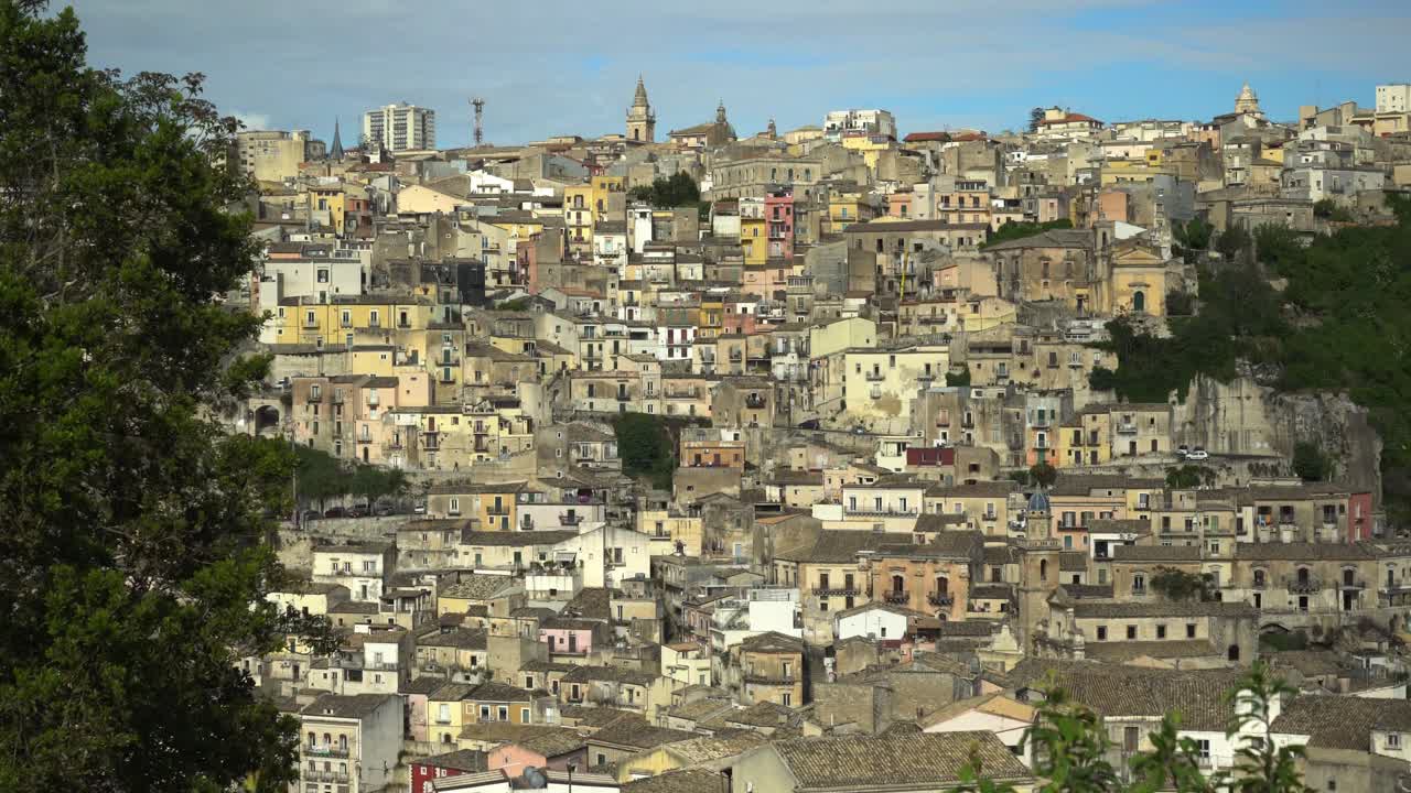 Veduta panoramica di Ragusa Superiore in Sicilia, Italia, città collinare con densi edifici storici, campanili e torri moderne tra verdi colline sotto un cielo sereno