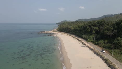 White-truck-drives-on-paved-road-by-sand-beach-on-Koh-Lanta,-Thailand