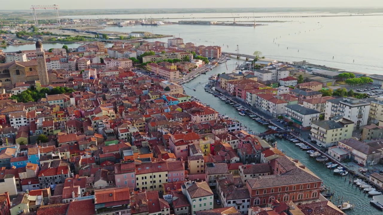 Riprese aeree cinematografiche con drone su Chioggia, Italia, che rivelano il centro storico, i tetti colorati, i canali e la Laguna di Venezia che risplendono nella calda luce serale dell'ora d'oro.