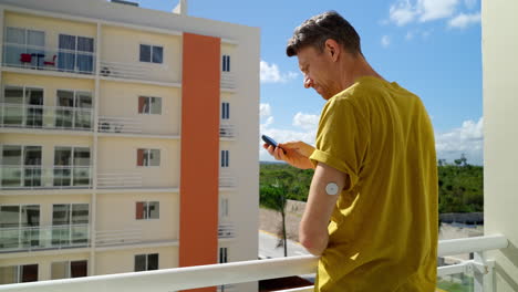 el viajero masculino comprueba sus niveles de glucosa en sangre en el brazo izquierdo con el sensor freestyle libre 2 en el balcón del hotel