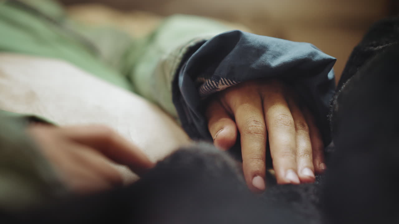 Close up of hand resting gently on soft surface, partially covered by worn jacket sleeve, belonging to someone lying down, conveying warmth and vulnerability