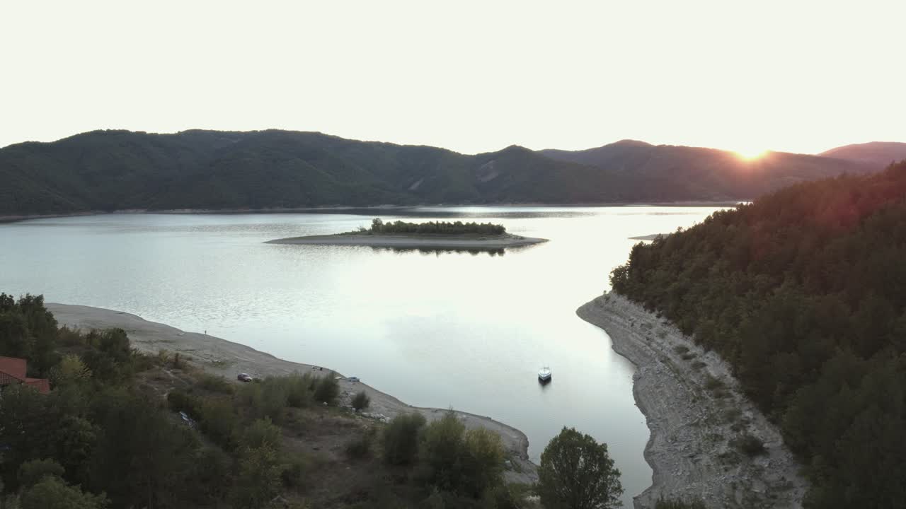 조용한 저수지 위에 아름다운 일몰, 멀리 작은 섬과 주변 언덕이 평화로운 풍경을 만니다.